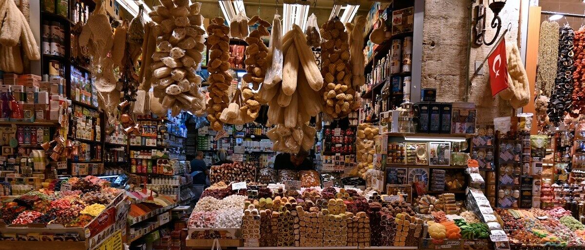 Uma banca de mercado movimentada, repleta de frutas secas, castanhas e artigos do dia a dia