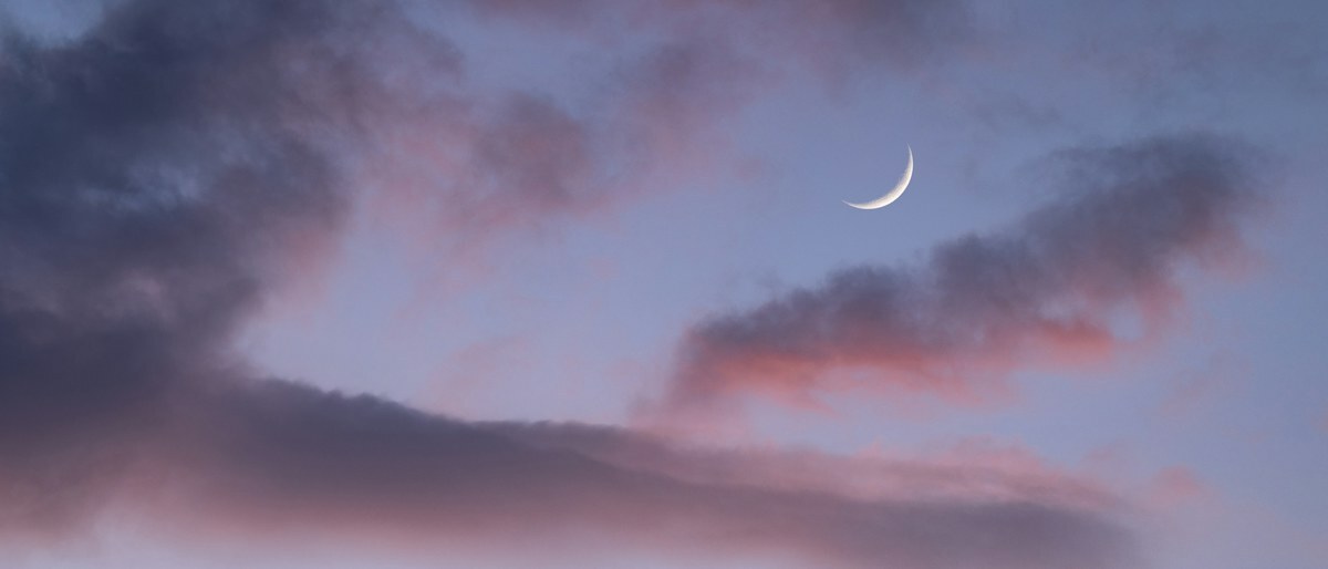 A thin crescent moon in a twilight sky with pink clouds