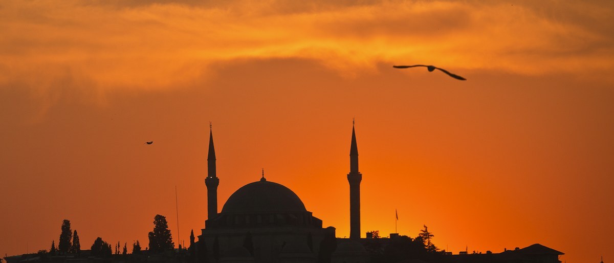 La sagoma della cupola e dei minareti di una moschea contro un cielo serale arancione