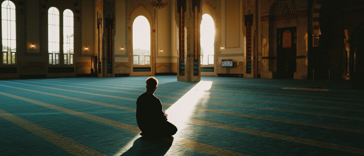 Ein Mann sitzt allein in einem sonnendurchfluteten Gebetssaal einer Moschee