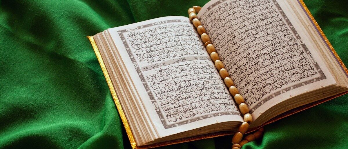 Ein aufgeschlagener Koran mit einer Gebetskette auf grünem Stoff