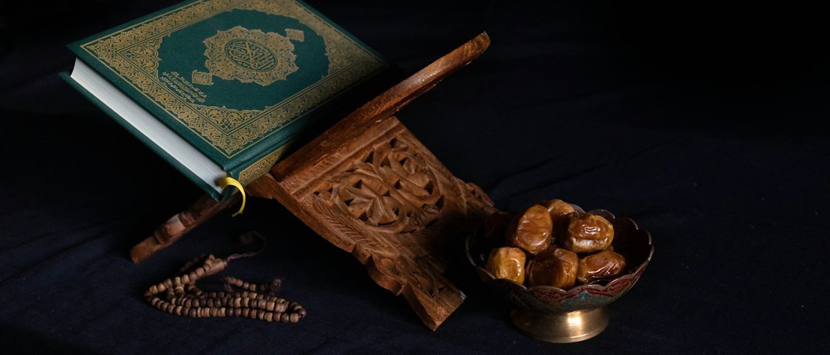 A Qur’an on a wooden stand beside a bowl of dates and prayer beads