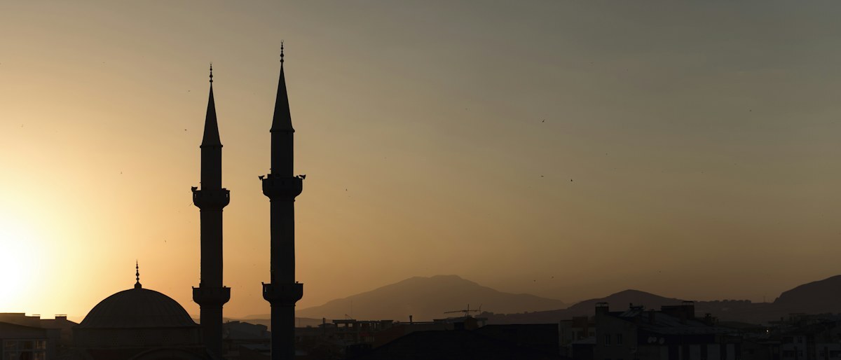 Two slender minarets in silhouette against a hazy sunset