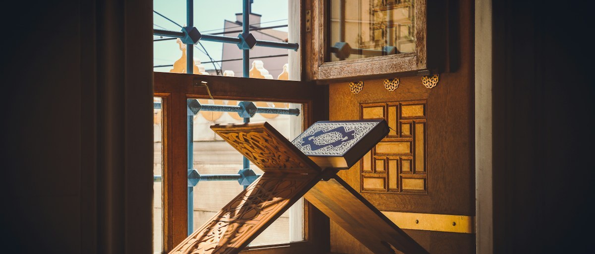 A wooden book stand holding an open book on a sunlit windowsill